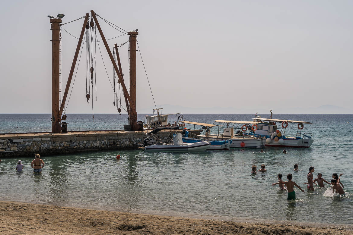 This image shows Moutsouna's port. Old facilities of the emery mines can be seen on the pier. In the foreground, chlidren play in the sea.
