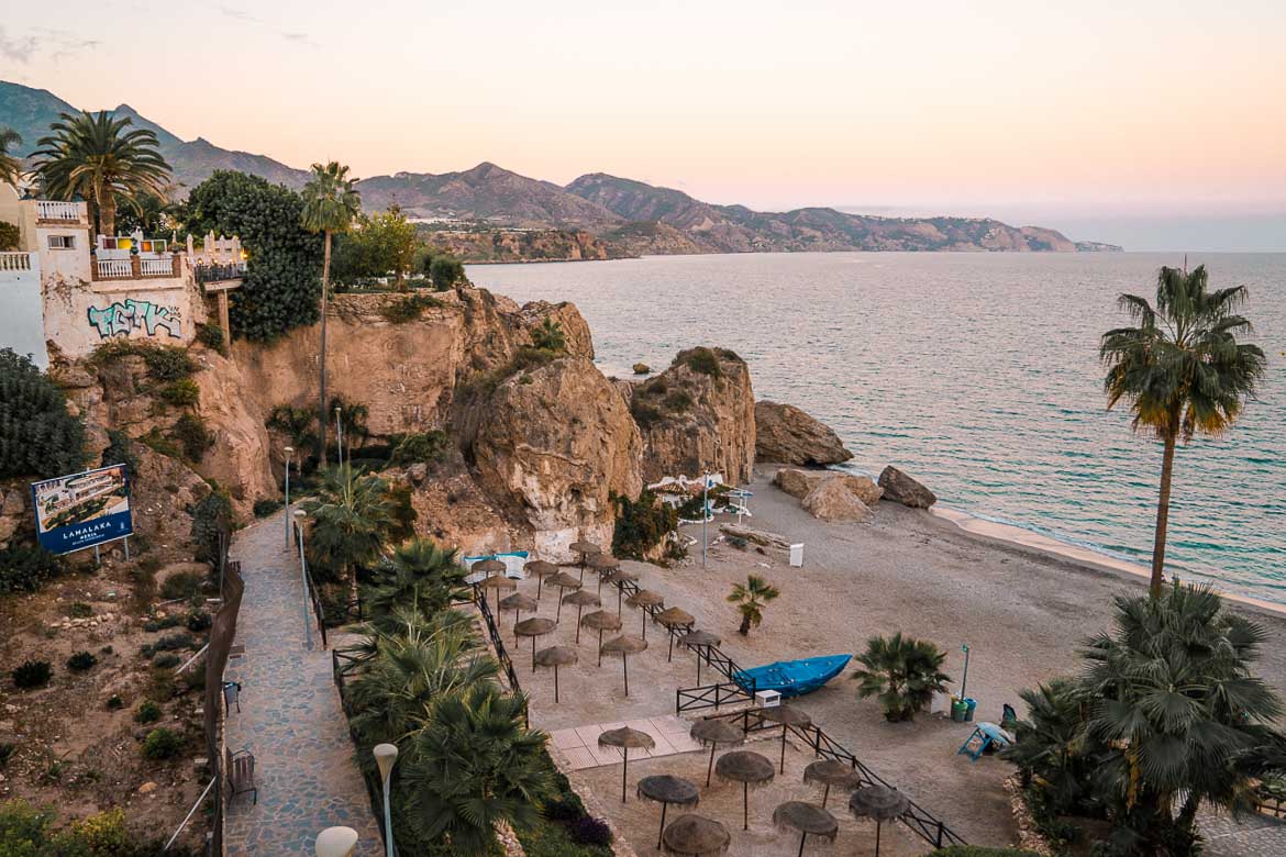 This image shows a beach with tall rocks and straw umbrellas. 