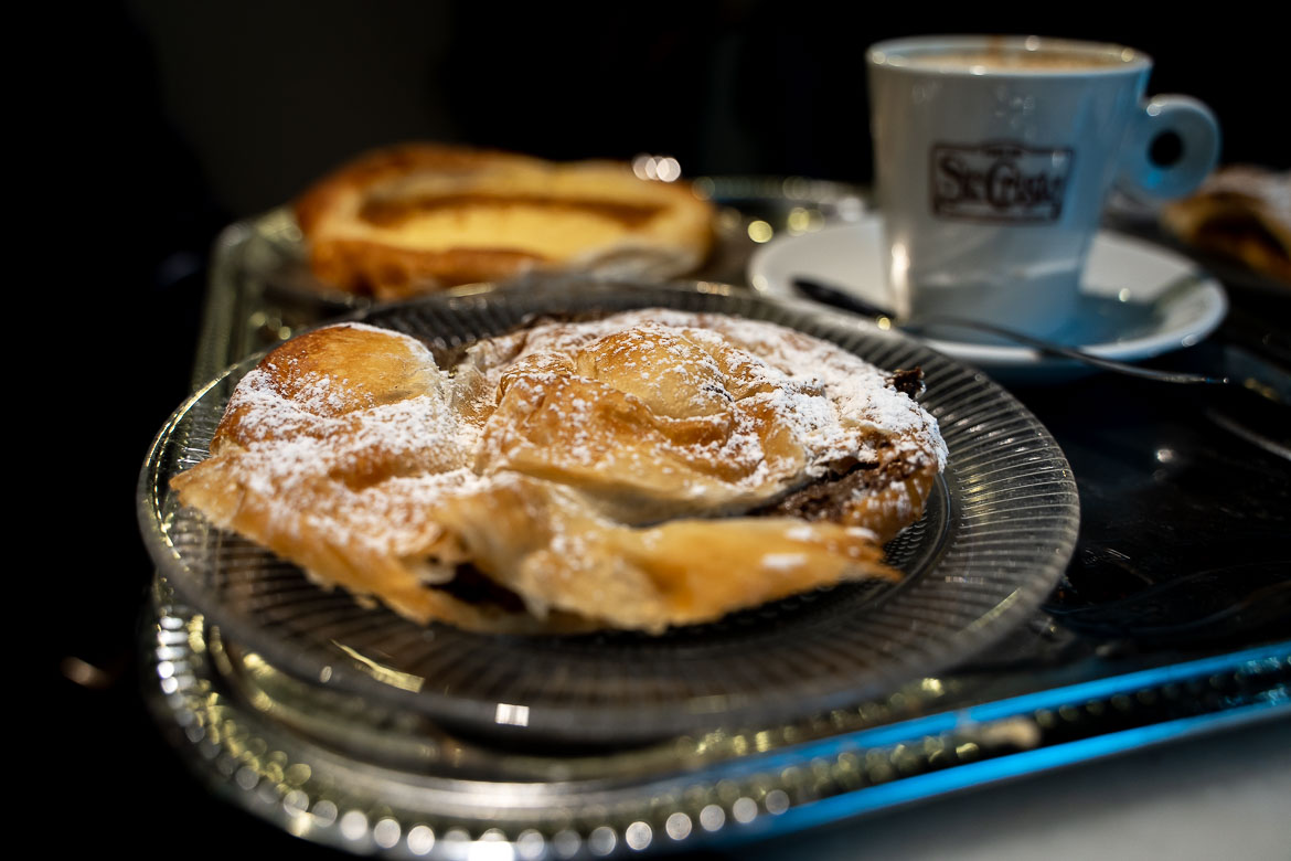 This is a close-up of a round pastry filled with chocolate cream. There's a cup of coffee in the background.