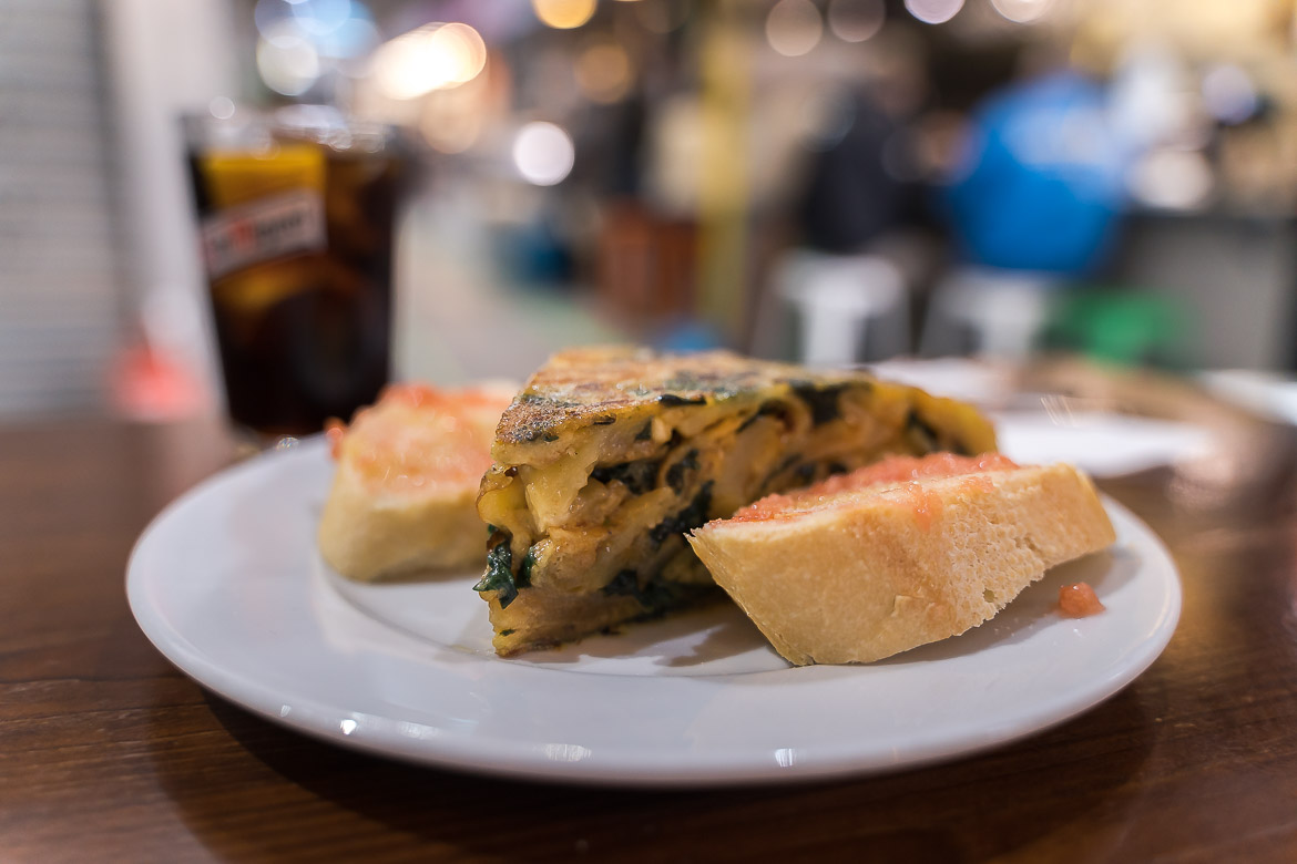 This is a close-up of a plate with a piece of Spanish omelette with spinach and two slices of bread with tomato and olive oil on top.