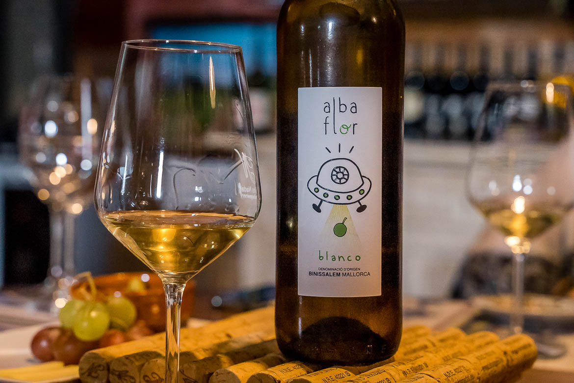 This is a close-up of a glass of white wine next to a bottle of white wine. There's a comic-like UFO on the bottle label and the name of the wine is Alba Flor.