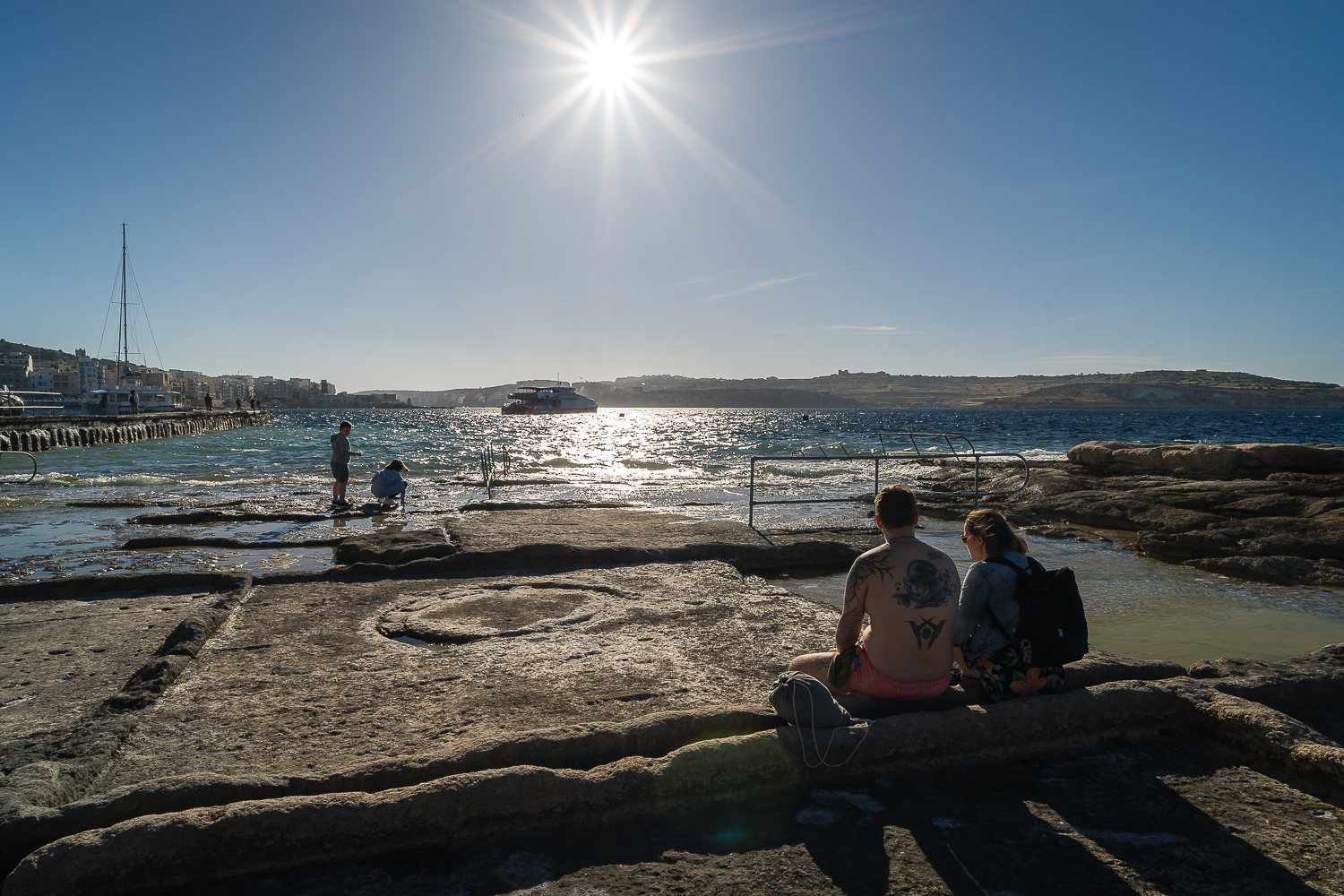 A couple is sitting in the salt pans by the sea at St. Paul's Bay.