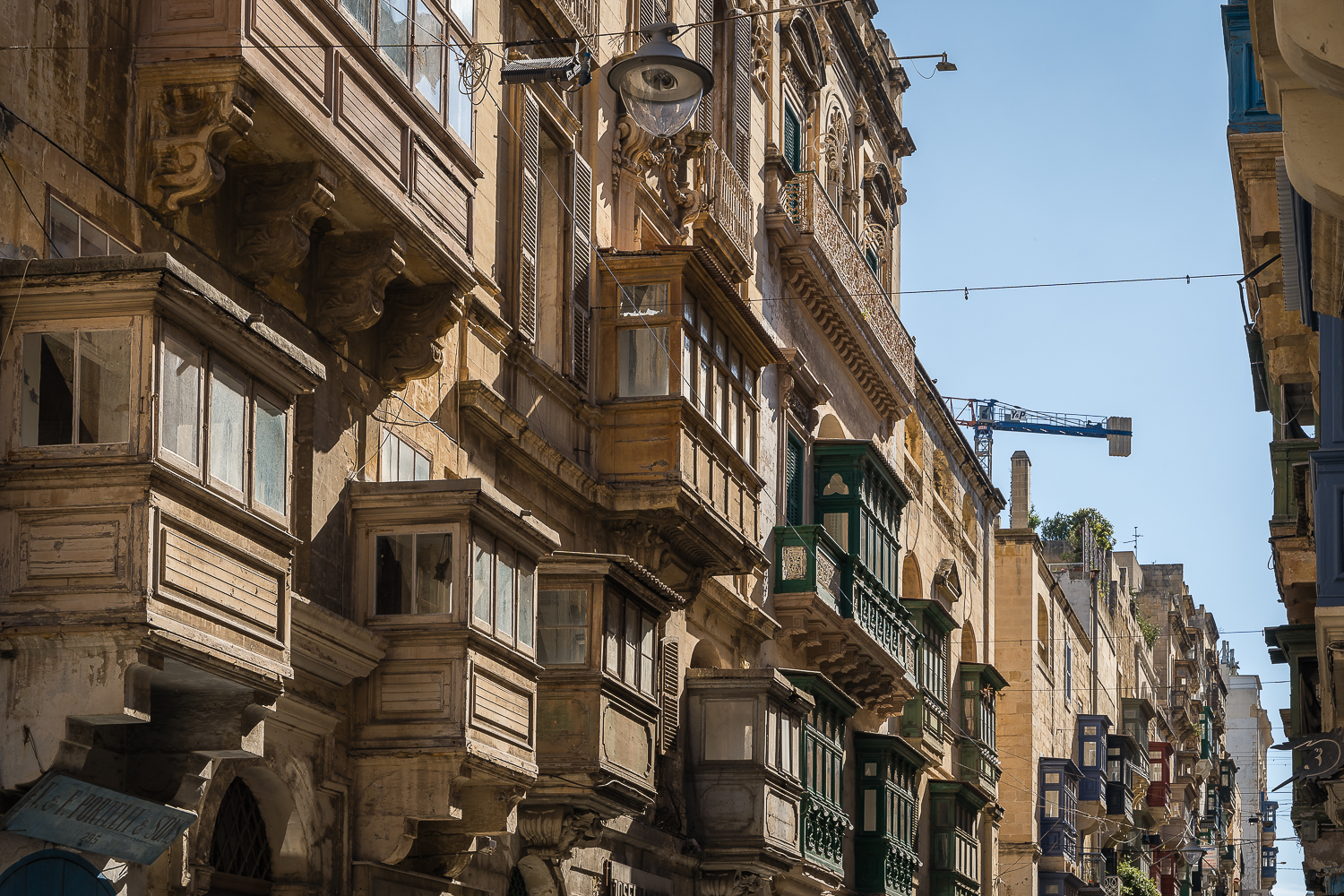 Old wooden balconies on facades along a street in Valletta.