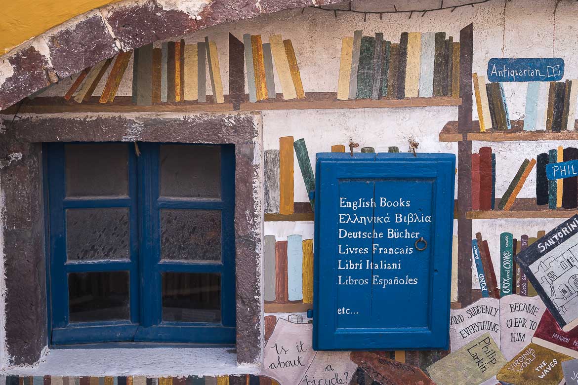 This image shows the facade of Atlantis Books. There's a blue window and a tiny blue door next to it that reads English books in many languages. There are also books painted on the wall.