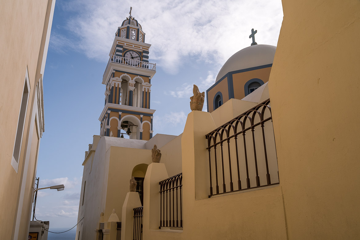 This is a close-up of the Roman Cathedral of St. John the Baptist in Fira. The bell tower is beautifully painted in yellow, blue and white.