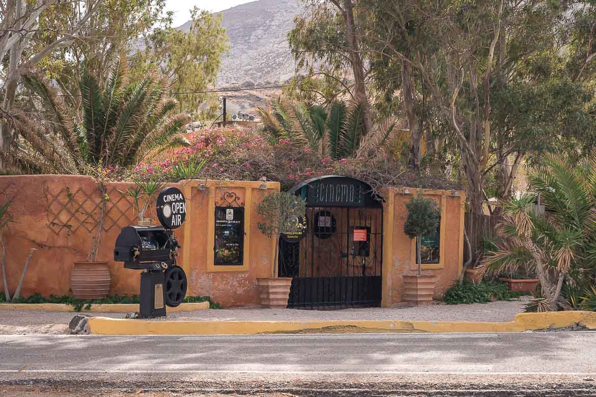 This image shows the entrance of Open Air Cinema Kamari, amidst trees and flowers.