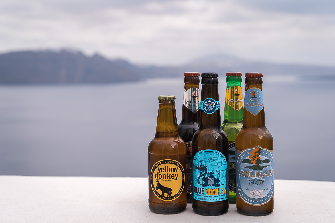 This image shows five different bottles of local beer with the Santorini caldera in the background.