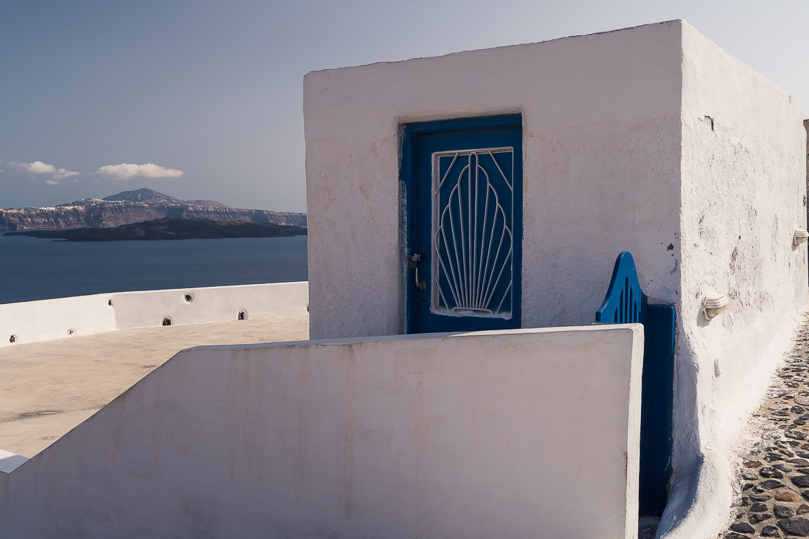 This image shows a white cubic house with a blue door in Thirassia.