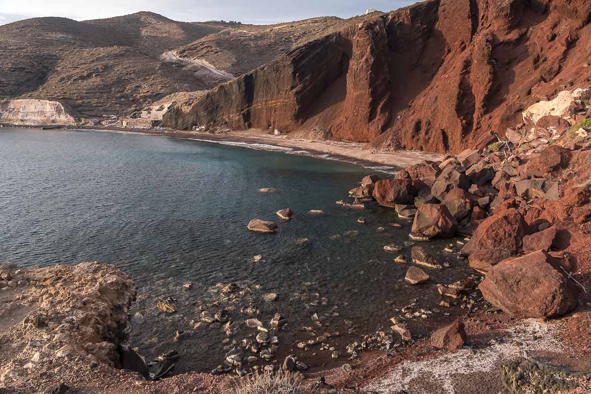 A panoramic view of the Red Beach, with red rocks reaching the dark blue sea.