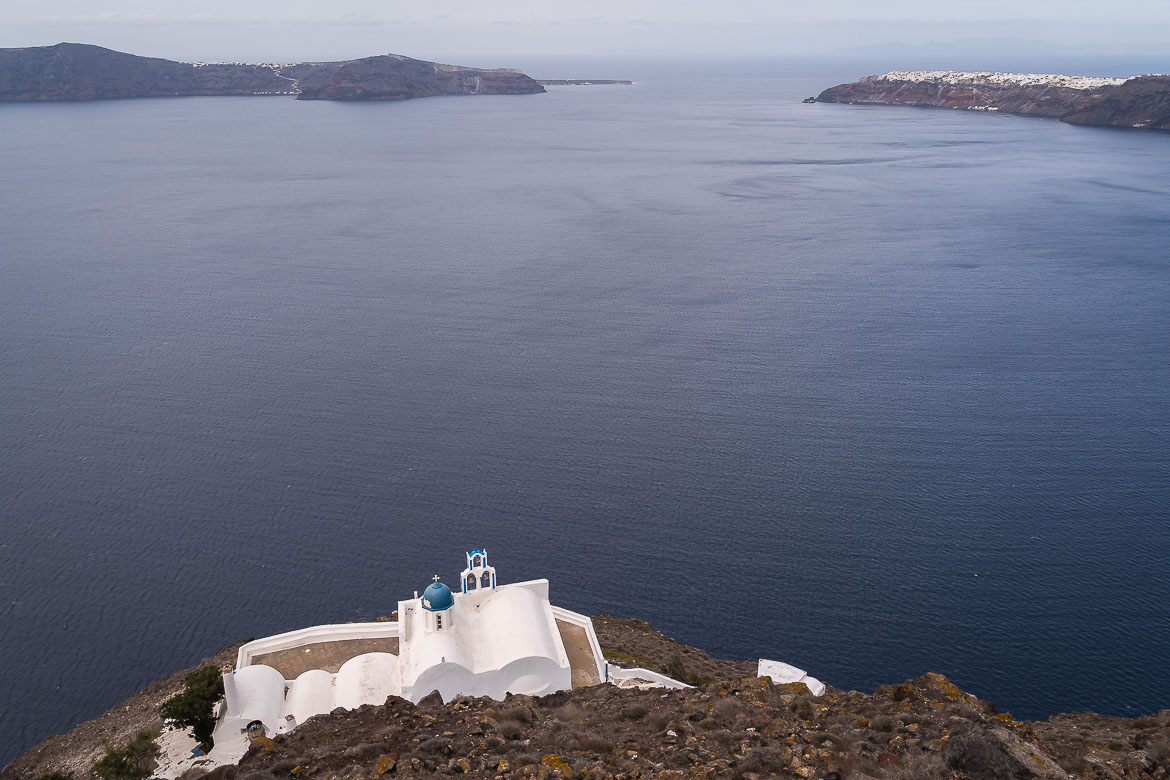 This photo shows the Chapel of Panagia Theoskepasti as it ceaselessly overlooks the divine blue of the Aegean Sea. In the distance, Oia looks like icing sugar on a cake.